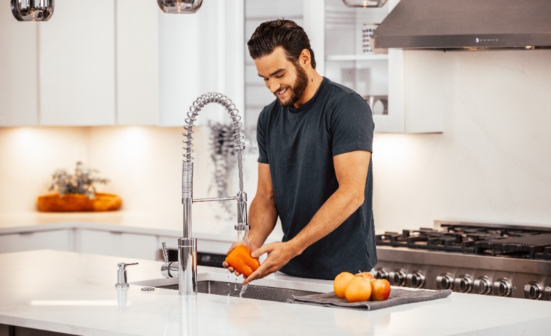 A man rinsing fresh produce under clean water in a bright modern kitchen